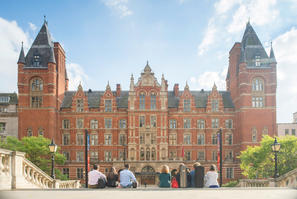 Students sat on the steps of the Royal Albert Hall, looking at the RCM's Blomfield Building with blue sky